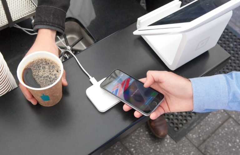 A customer holds an iPhone near a small card reader to pay at a coffee counter