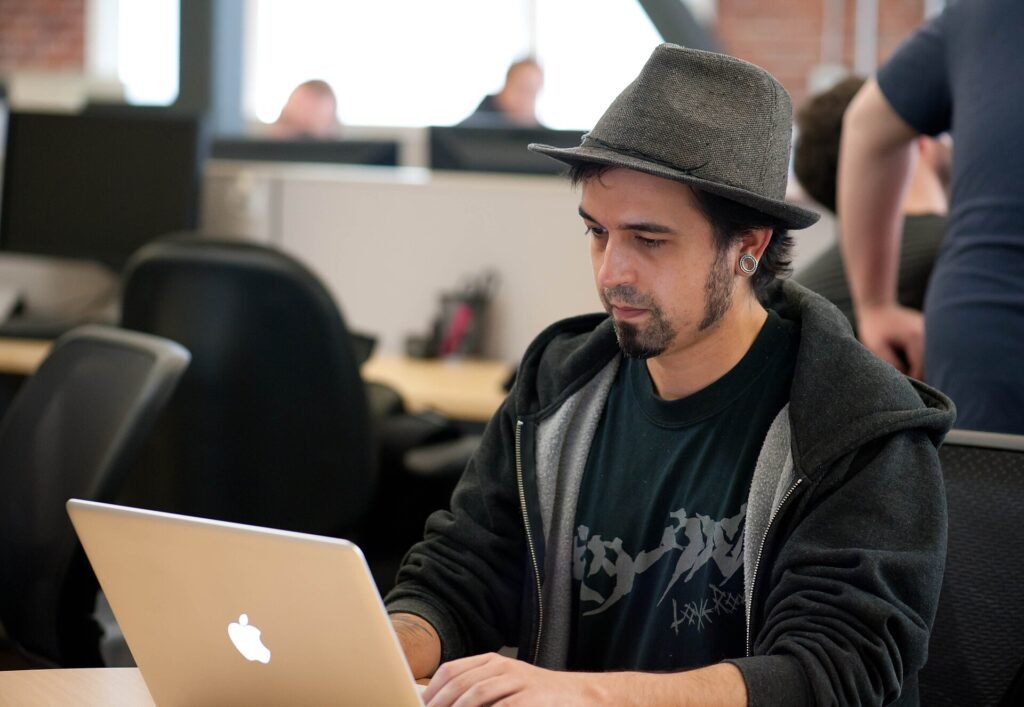 A developer in a grey hat working on a laptop in an open-plan office