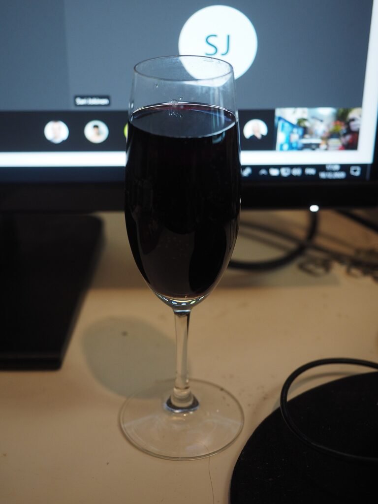 A glass of red wine in front of a monitor showing a Microsoft Teams video meeting
