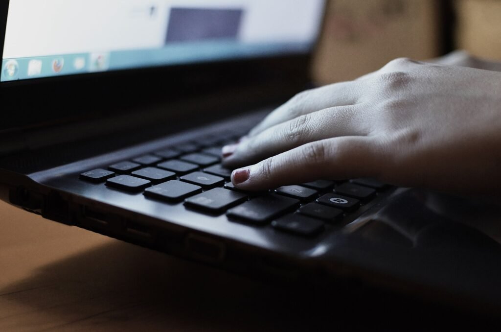 A hand typing on a laptop keyboard next to a notebook