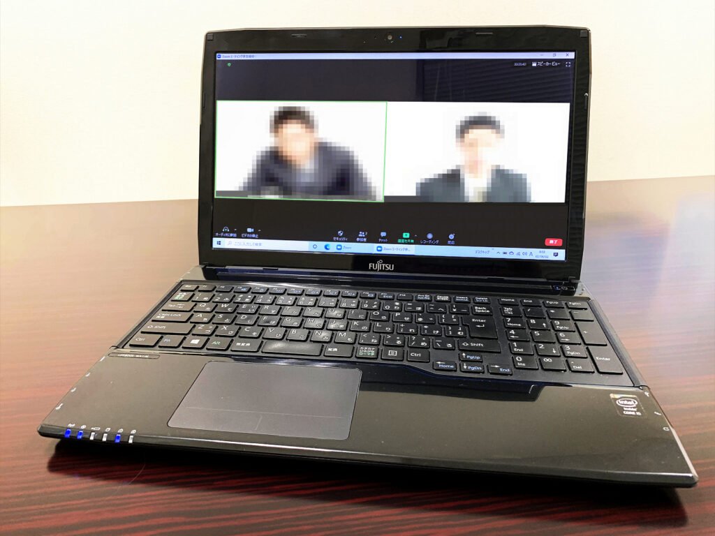 A laptop on a desk showing a video call with two blurred participants