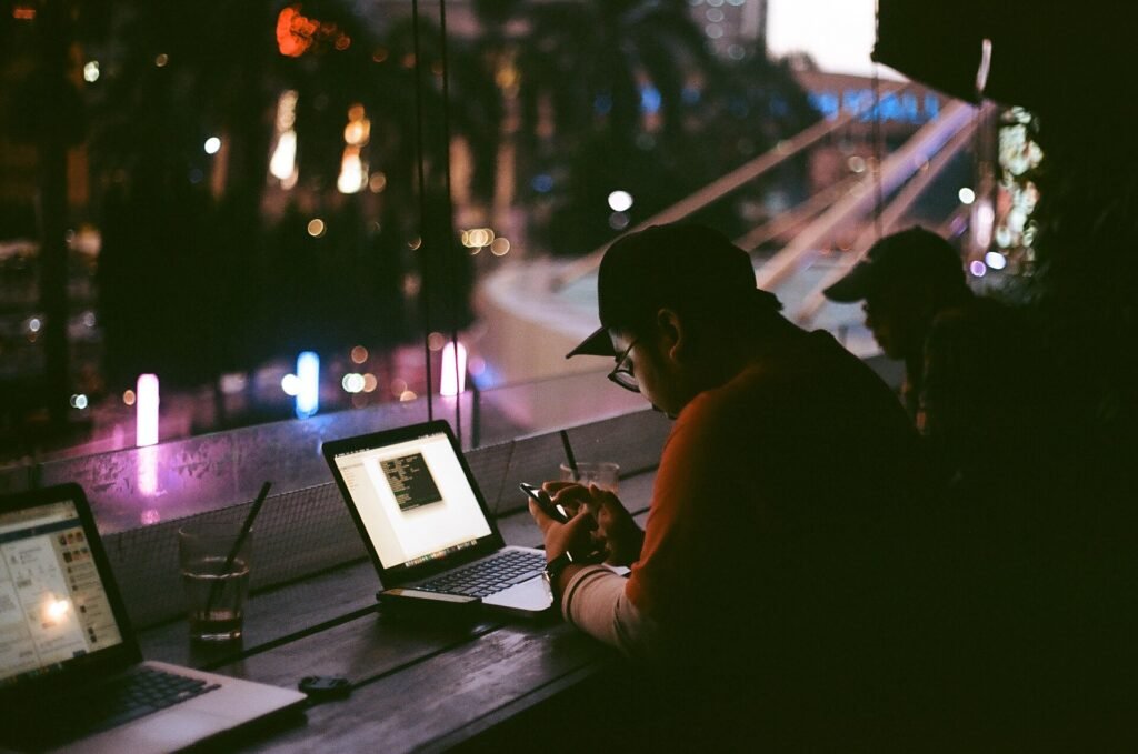 A person working on a laptop at a dimly lit bar counter at night next to other laptops