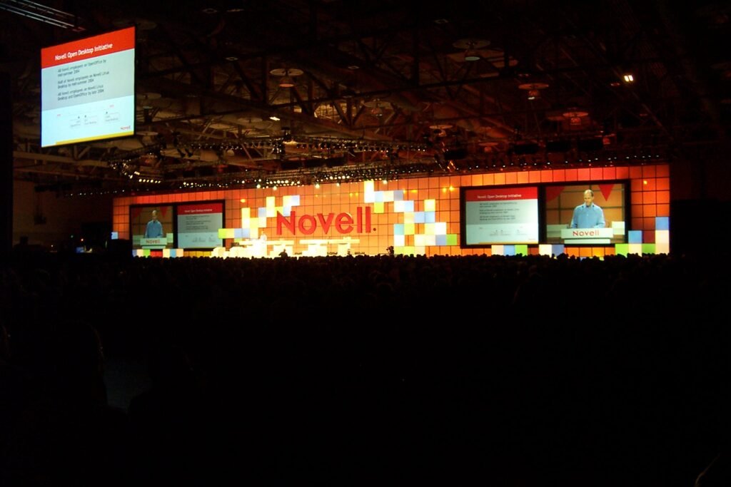 A speaker on a conference stage in front of large projected presentation slides