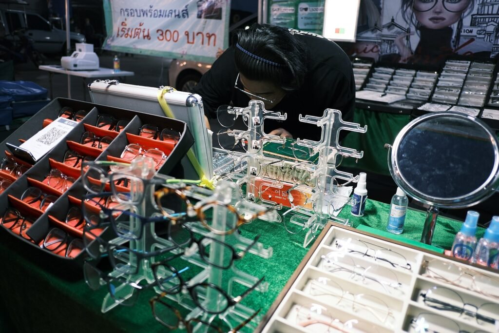 A street vendor arranging eyeglasses and sunglasses on an outdoor market stall