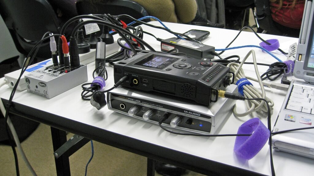 A table of audio recording equipment including a digital recorder, mixer and cables used for a webinar and podcast