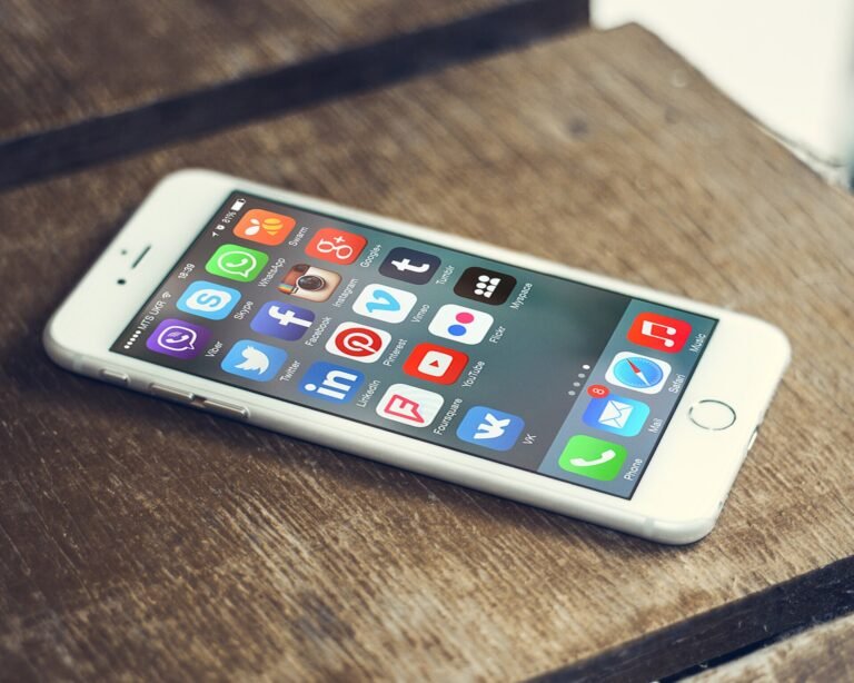 A white smartphone on a wooden table showing a home screen full of social media app icons