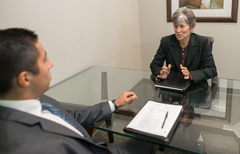 A woman interviews a young man across a desk in an office