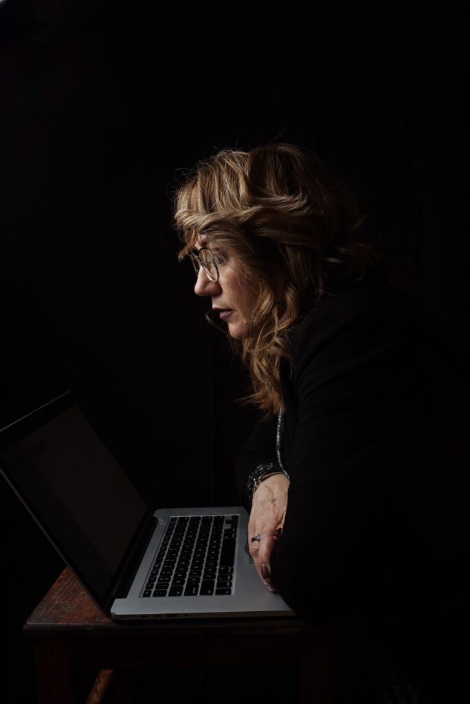 A woman working on a laptop at a desk in a dimly lit room