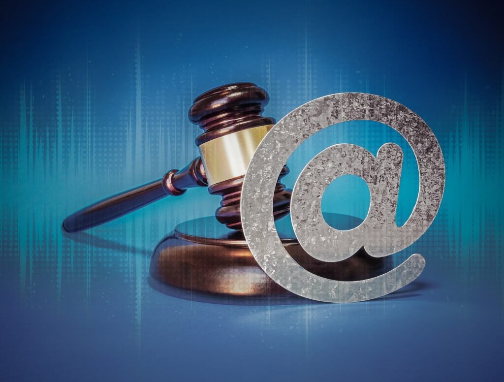 A wooden judge's gavel beside a large metallic @ symbol on a blue background