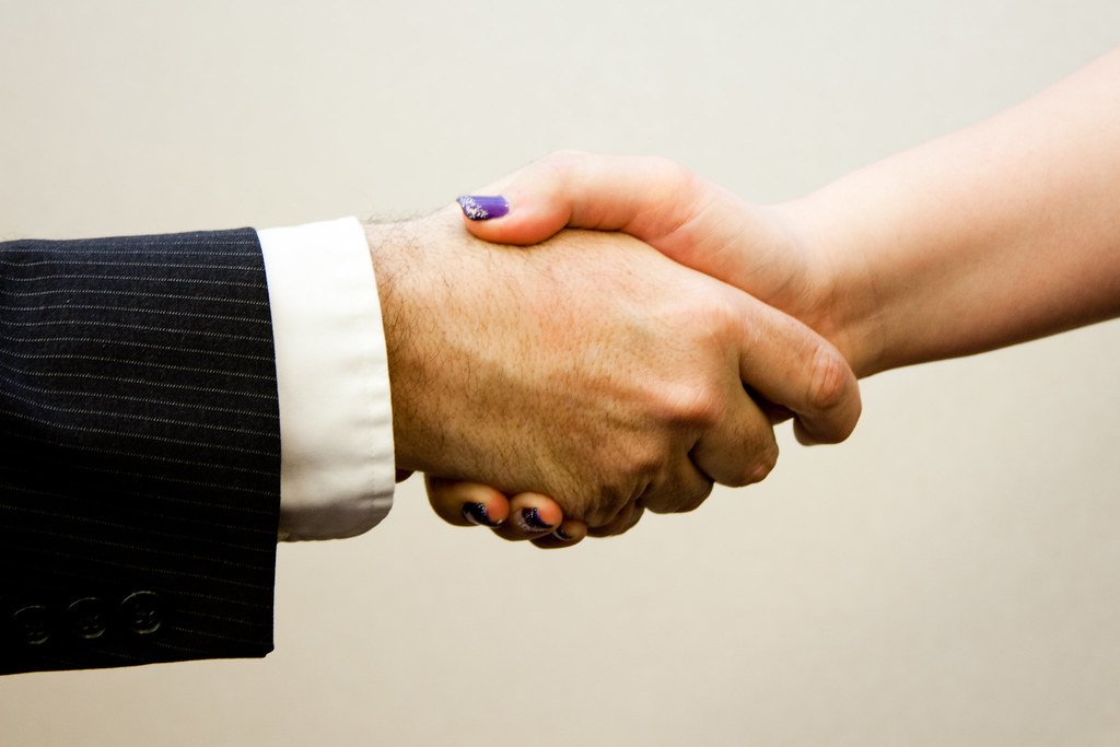 Close-up of a man and a woman shaking hands across a table