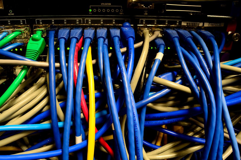 Dense bundle of blue, grey, green, red and yellow Ethernet cables plugged into a network switch