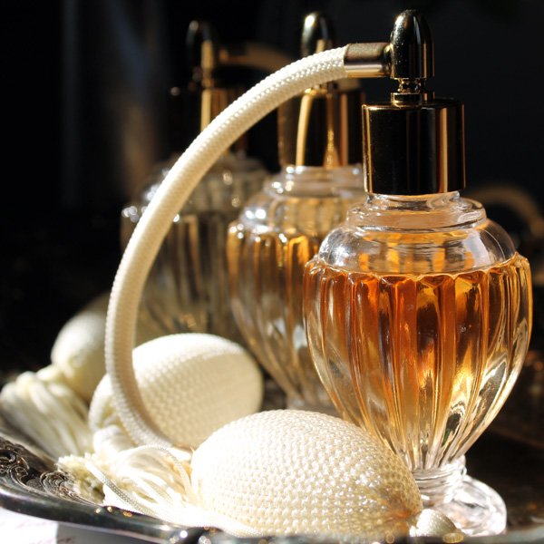 Glass perfume bottles with amber liquid and a vintage bulb atomizer on a silver tray
