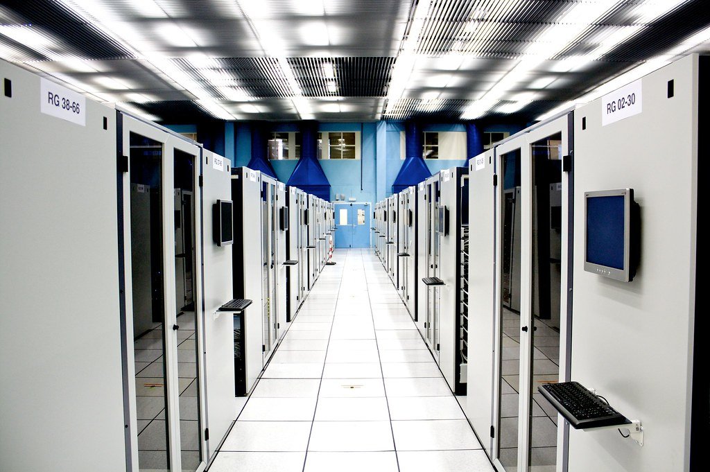 Long aisle of white server racks under bright ceiling lights in the CERN server room