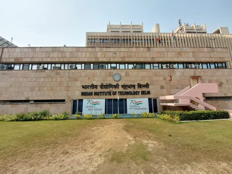 Main building of IIT Delhi with its name in Hindi and English above a lawn