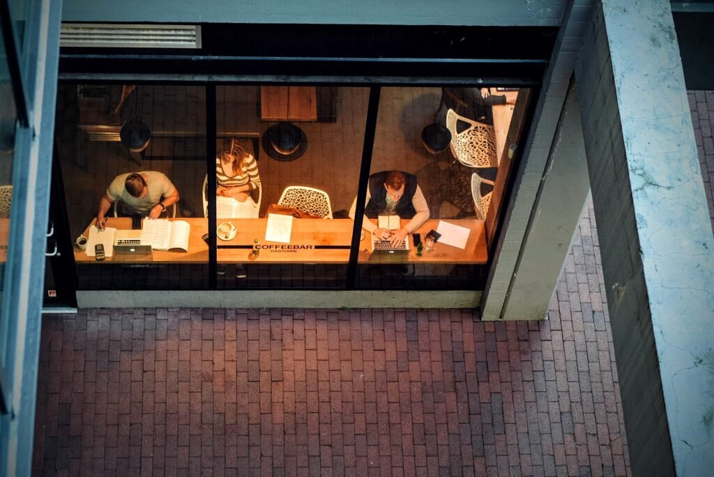 People working on laptops at a long table, seen through a window from above