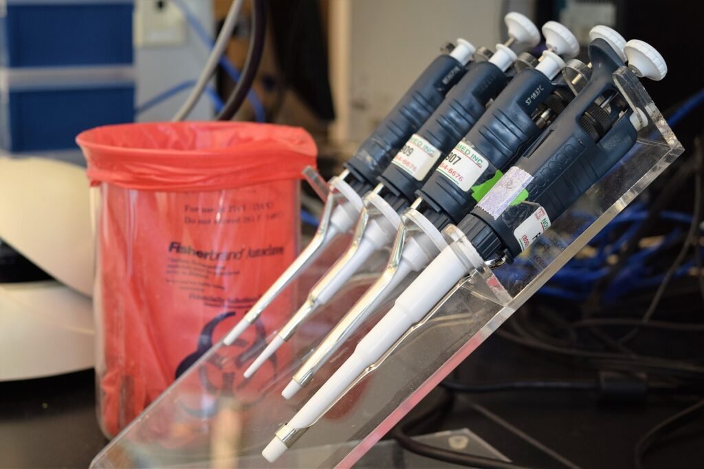 Row of adjustable laboratory pipettes on a clear stand on a lab bench