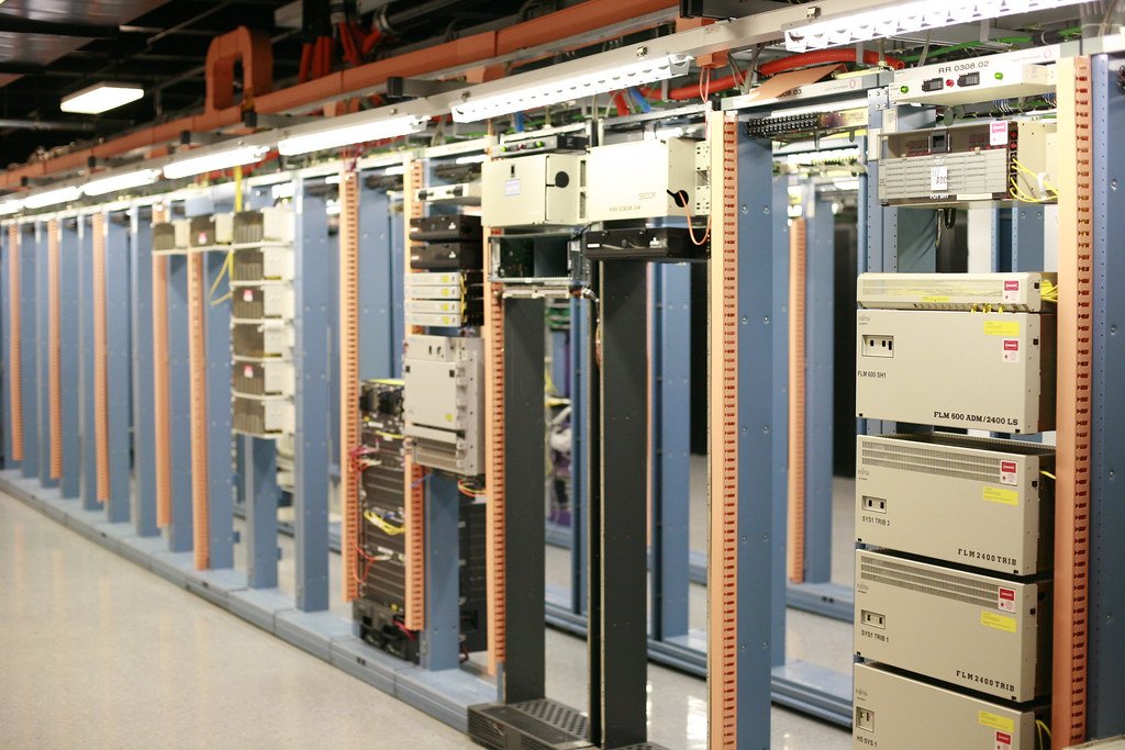 Rows of telecom and server equipment racks in a brightly lit data centre