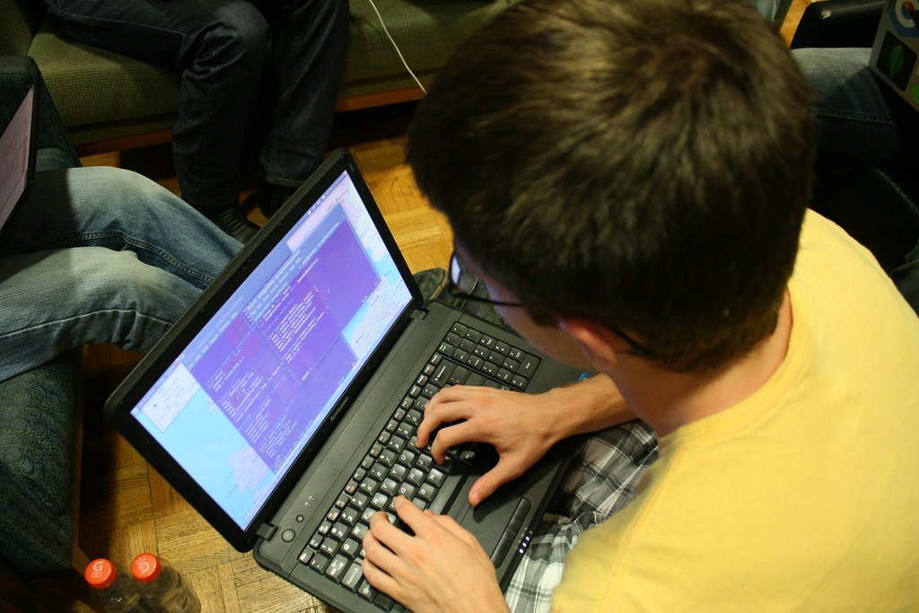 Students coding on laptops around a table at a hackathon