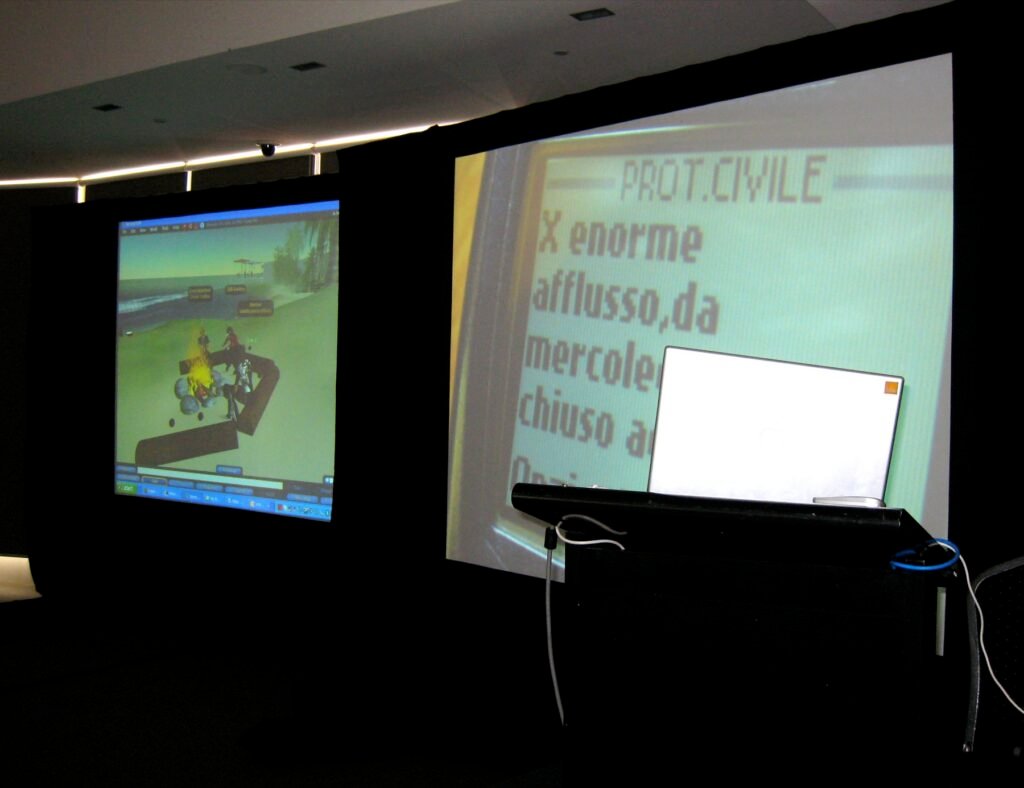 Two projection screens in a dark auditorium showing a presentation and a live video feed